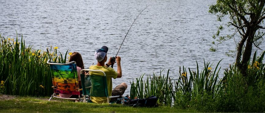 two people fishing from a grassy shore