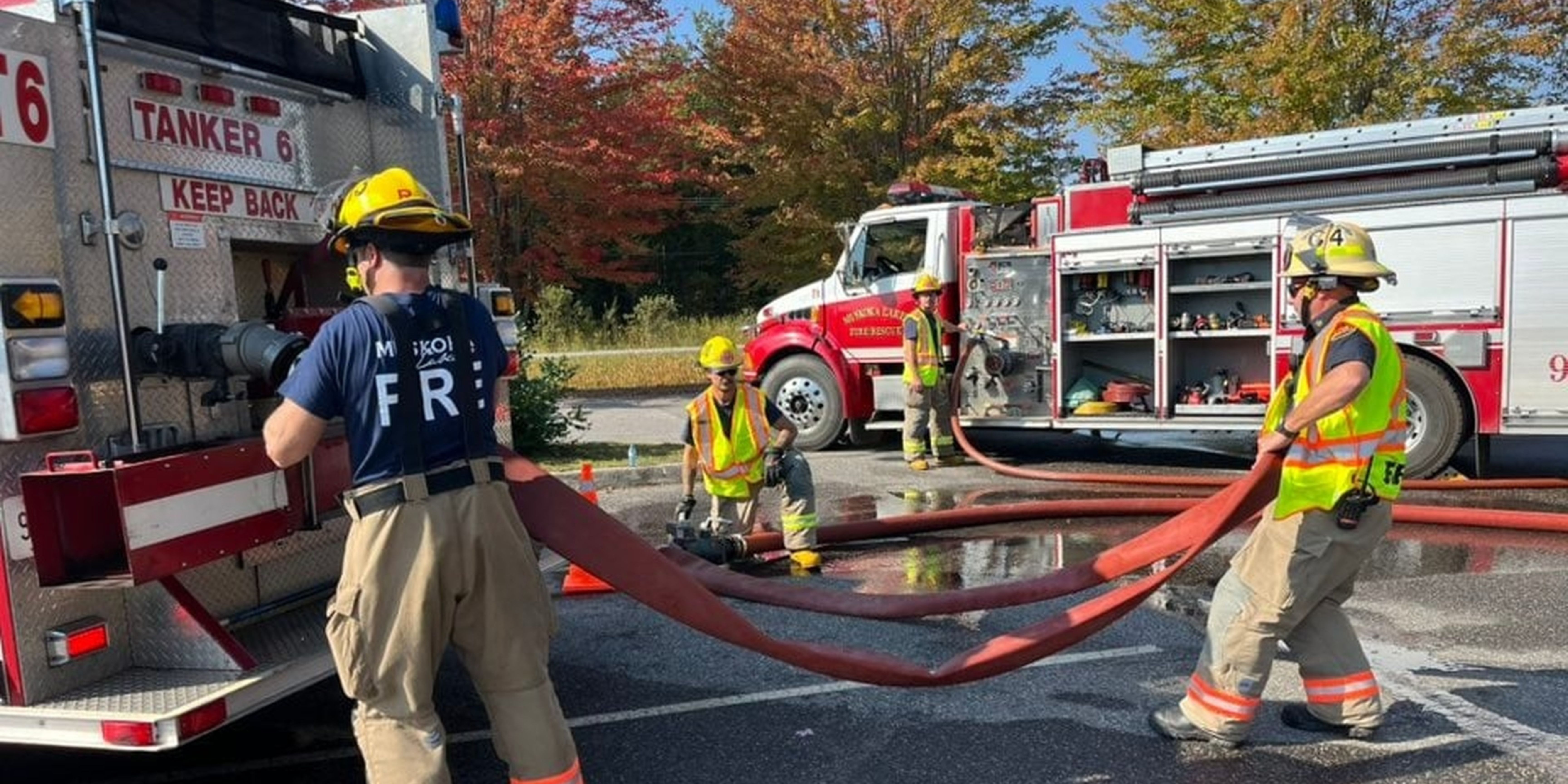 Four firefighters managing a hose surrounded by two firetrucks