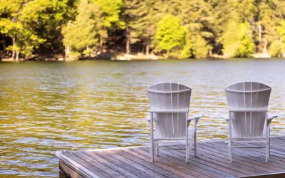 Image of Muskoka chairs on dock, facing lake and trees 