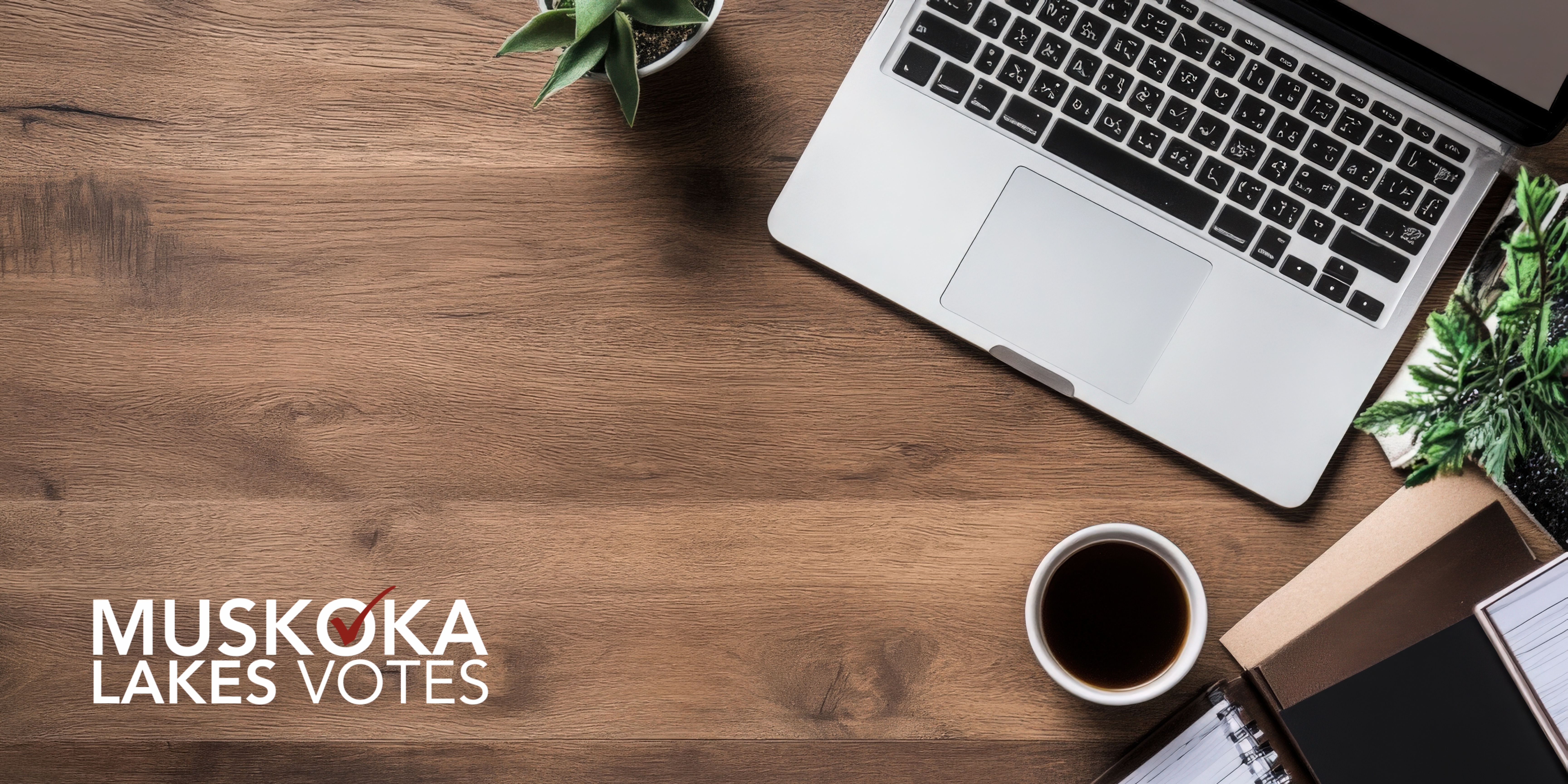 Aerial view of a desk with a computer and coffee and muskoka lakes votes logo