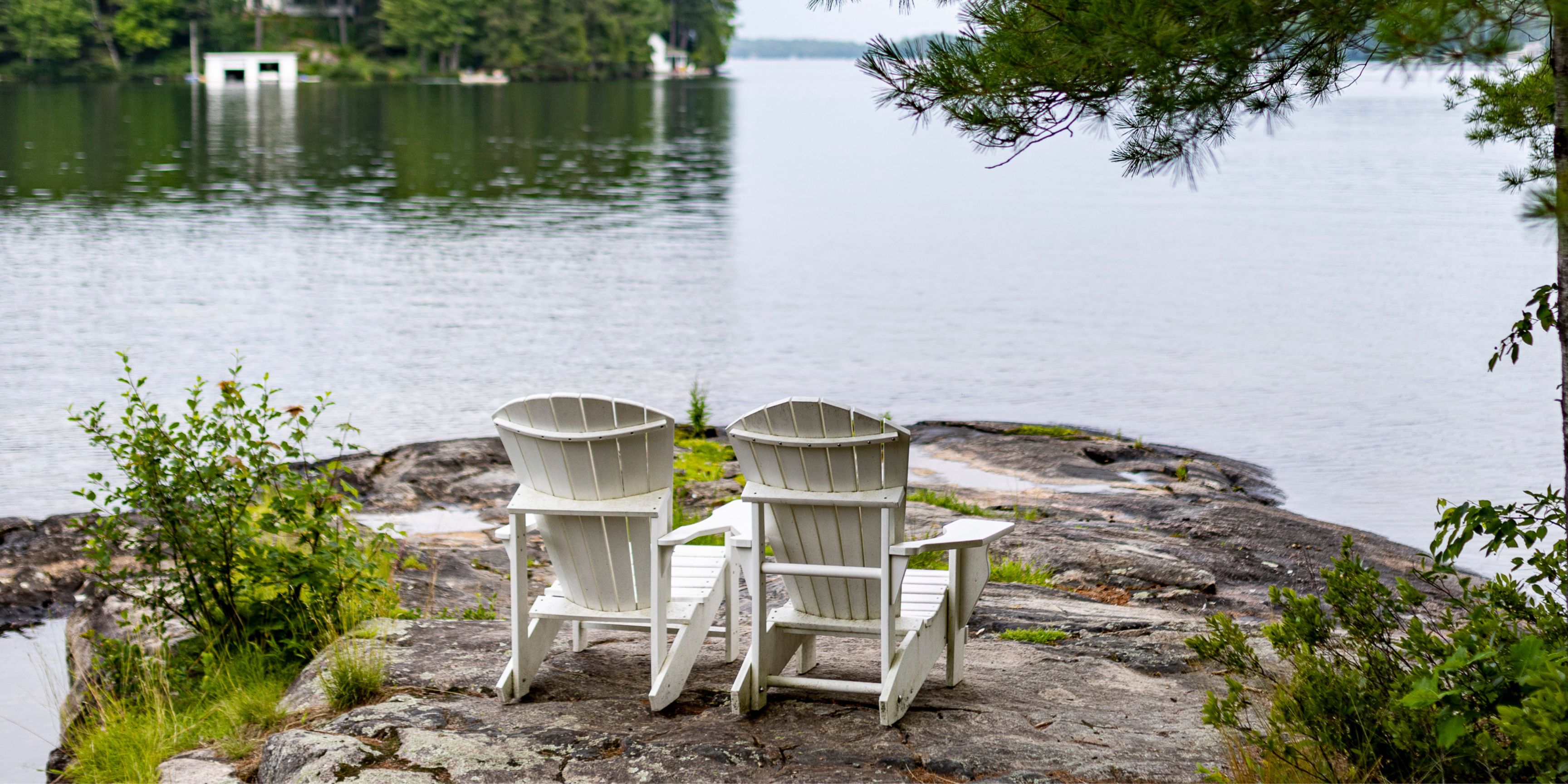 Two Muskoka chairs on a rock facing the lake