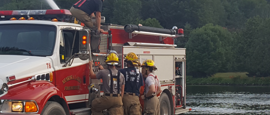 Firefighters on and beside a fire truck at a lake